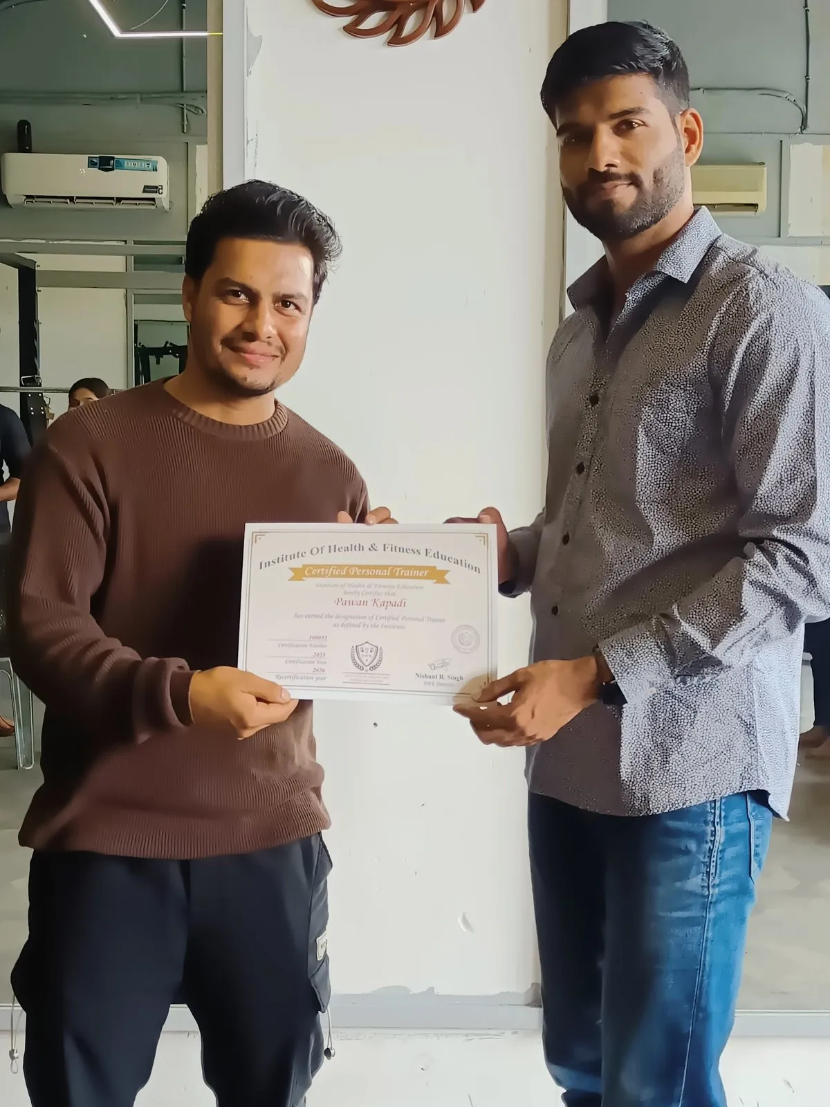 Smiling graduate receiving an IHFE Certified Personal Trainer certificate at the gym