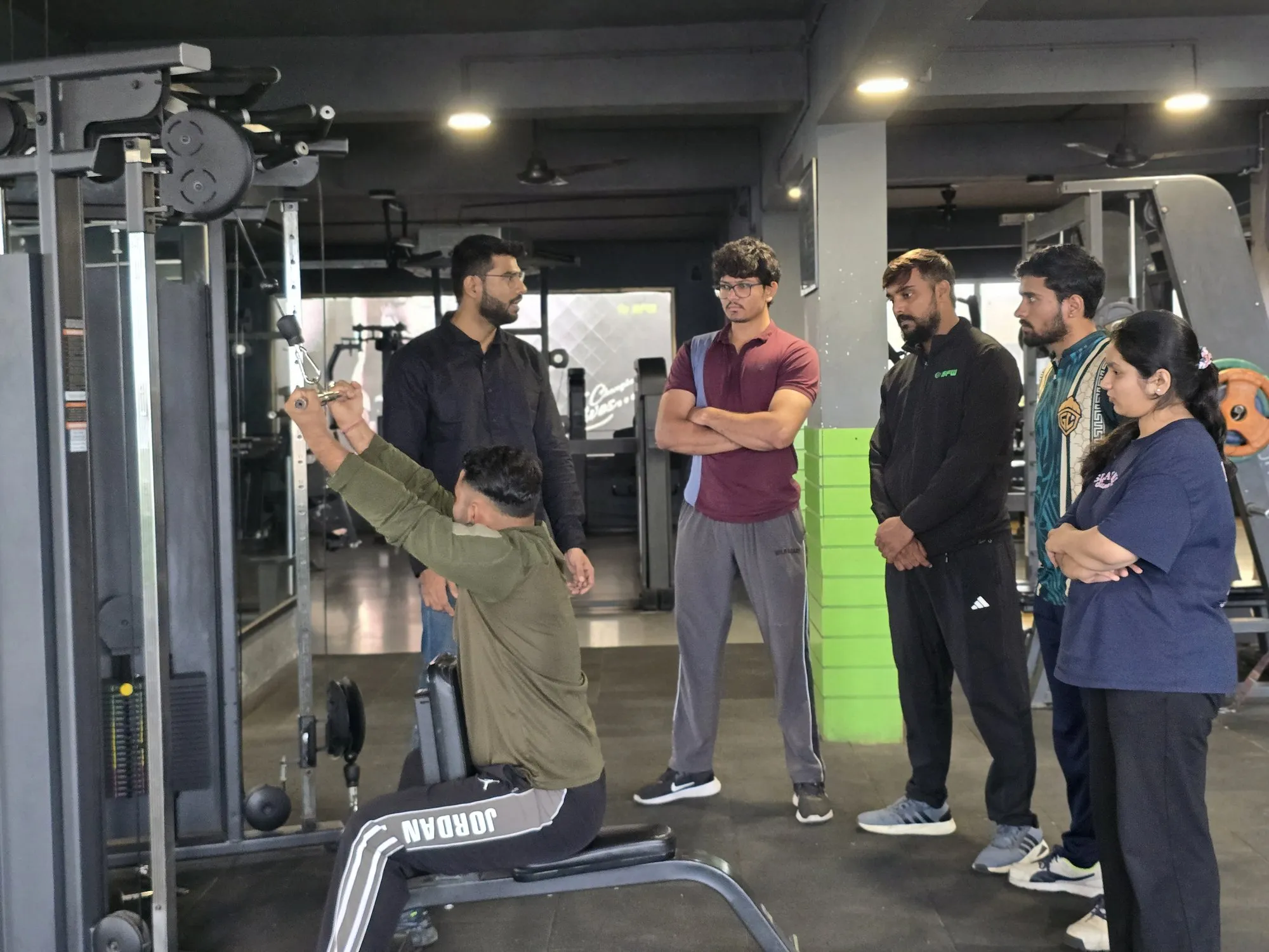 IHFE instructor explaining seated cable pulldown form to trainee personal trainers during a practical fitness session